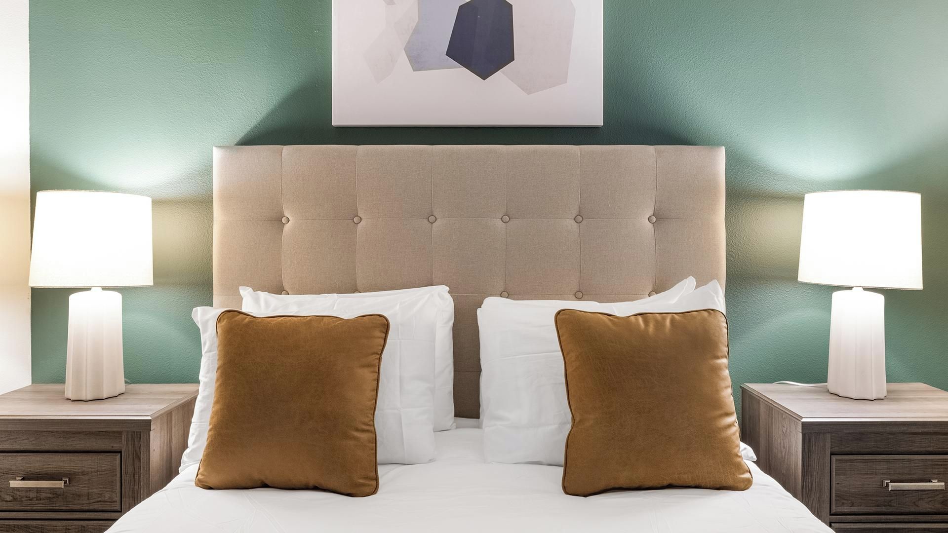Une chambre à coucher avec une tête de lit capitonnée, deux tables de chevet avec des lampes et deux coussins marron.
