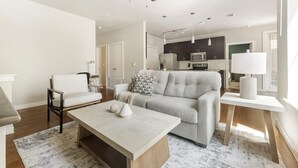 Ein modernes Wohnzimmer mit Sofa, Couchtisch und Essbereich, im Hintergrund eine Küche.