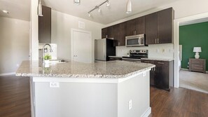 A modern kitchen with granite countertops, stainless steel appliances, and dark wood cabinets. - Landing | Spectacular 2BD, Pool, Gym (Austin)