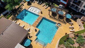 A rooftop pool area with two separate pools, lounge chairs, umbrellas, and a small hot tub. - Landing | Modern 2BD, Pool, Gym (Austin)