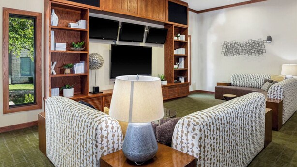 A living room with a large flat-screen TV, wooden shelving, patterned sofas, and a lamp. - Landing | Modern 2BD, Pool, Gym (Austin)