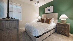 Ein Schlafzimmer mit einem Bett, Nachttischen, einer Kommode, einem Deckenventilator und einem Fenster.