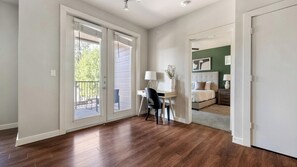 A room with a wooden floor, a desk with a chair, a bed with a headboard, and a green accent wall. - Landing | Stylish 2BD, Pool, Gym (Austin)