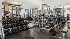 Een sportschool met fitnessapparatuur, rekken voor gewichten en een bank.