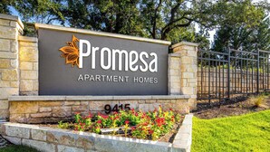 Een bordje voor Promesa Apartment Homes, met een stenen muur en een metalen poort.