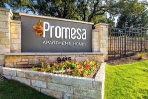 Schild für Promesa Apartment Homes, mit einer Steinmauer und einem Metallgitter.