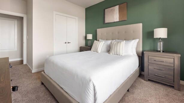 A bedroom with a large bed, two bedside tables, a nightstand, a wardrobe, and a wall-mounted artwork. - Landing | Beautiful 2BD, Pool, Gym (Austin)