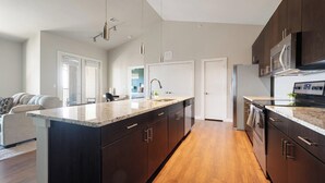 A modern kitchen with dark wood cabinets, a granite countertop, and stainless steel appliances. - Landing | Beautiful 2BD, Pool, Gym (Austin)