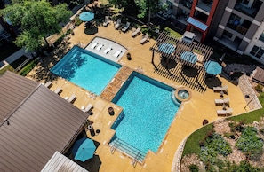 A rooftop pool area with two separate pools, lounge chairs, umbrellas, and a small hot tub. - Landing | Beautiful 2BD, Pool, Gym (Austin)