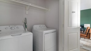 A laundry room with two white washing machines and a door leading to another room. - Landing | Stylish 1BD, Pool (Houston)
