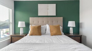 A bedroom with a bed, two bedside lamps, a headboard, and a wall painting. - Landing | Stylish 1BD, Pool (Houston)