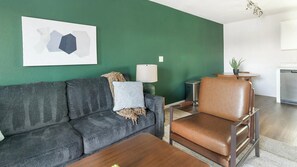 Una sala de estar moderna con una pared de acento verde, un sofá gris, un sillón de cuero marrón, una mesa de centro de madera y una mesita auxiliar con una lámpara.