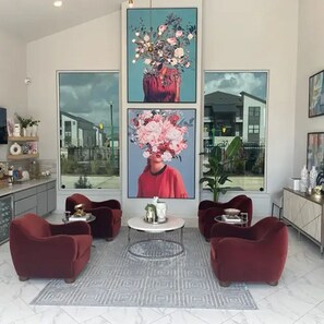 A modern living room with red sofas, a round coffee table, and large framed floral artwork on the walls. - Landing | Spectacular 1BD, Pool (Houston)