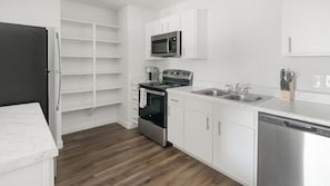 A modern kitchen with white cabinetry, a stainless steel refrigerator, a built-in microwave, a gas stove, and a dishwasher. - Landing | Stylish 1BD, Pool (Houston)
