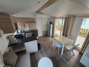 Eine kompakte Küche mit Herd, Mikrowelle und Kühlschrank, ein Essbereich mit Tisch und Stühlen sowie Blick auf eine hölzerne Terrasse.