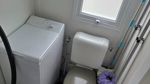 Een kleine, praktische badkamer met toilet, een wasmachine en een dweil.