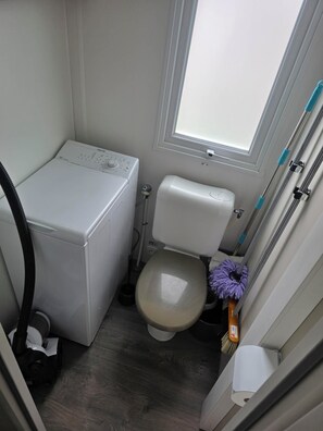 Ein kleines, kompaktes Badezimmer mit Toilette, einer Waschmaschine und einem Mop.