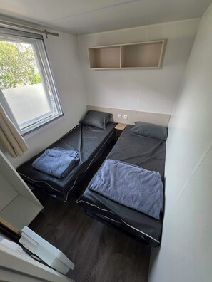 Ein kleines Zimmer mit zwei Einzelbetten, einem kleinen Tisch und einem Fenster mit Vorhängen.