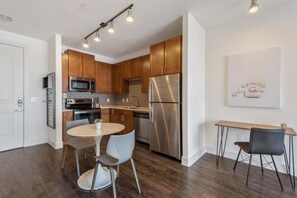 A modern kitchen with stainless steel appliances, wooden cabinets, a dining area with a round table and chairs, and a wall-mounted light fixture. - Landing | Incredible 1BD, Pool (Houston)