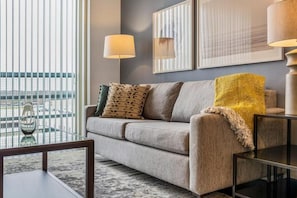 A modern living room with a sofa, a coffee table, and two lamps. - Landing | Incredible 1BD, Pool (Houston)