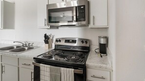A kitchen with a stainless steel stove, a microwave, and a coffee maker. - Landing | Chic 1BD, Pool (Houston)