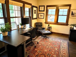 Ein Homeoffice mit Schreibtisch, Computer, Stuhl und einem großen Fenster mit Jalousien.