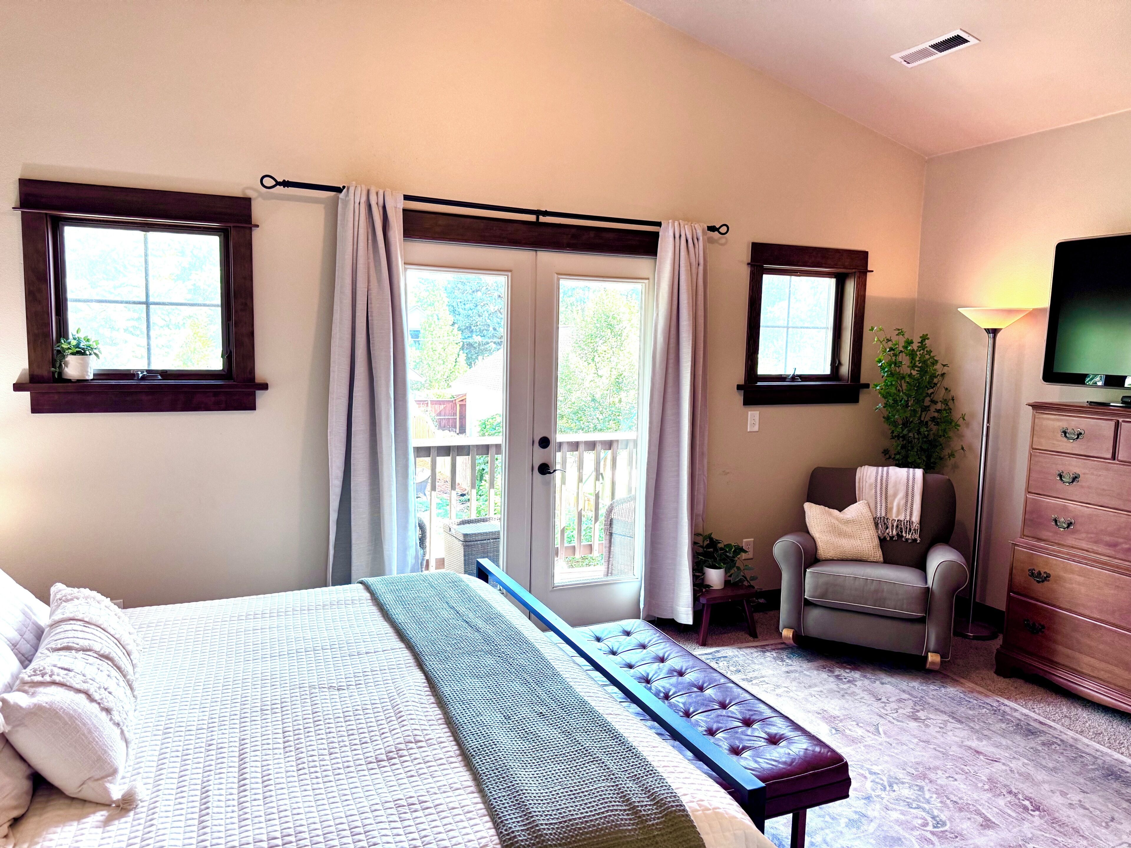 A bedroom with a bed, a bench, a chair, a dresser, and a television.