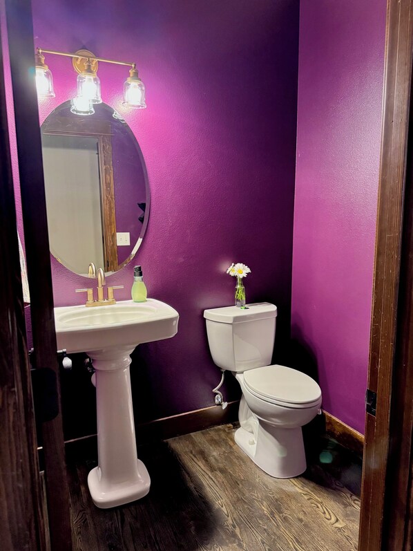 Un baño con lavamanos pedestal, inodoro y espejo con iluminación.