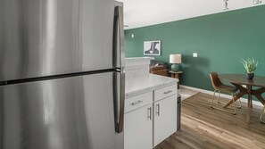 Eine Küche mit einem Edelstahl-Kühlschrank, weißen Schränken, einer Marmorarbeitsplatte und einem Essbereich mit Tisch und Stühlen.