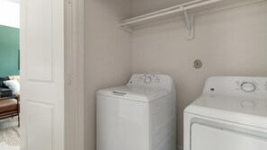 A laundry room with a front-loading washer and dryer, a white door, and a green wall. - Landing | Chic 1BD, Pool (Houston)