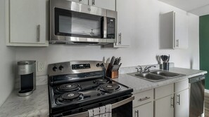 A modern kitchen with stainless steel appliances, a built-in microwave, a stovetop, and a double sink. - Landing | Chic 1BD, Pool (Houston)