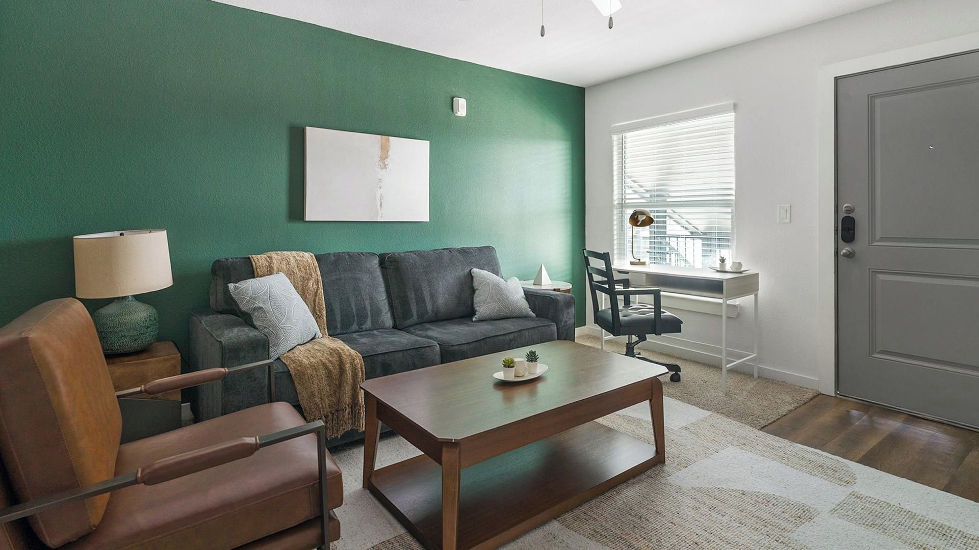 Un salon moderne avec un mur d’accent vert, un canapé, une table basse et un bureau avec une chaise.