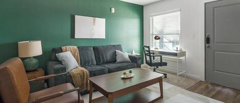 Un salon moderne avec un mur d’accent vert, un canapé, une table basse et un bureau avec une chaise.