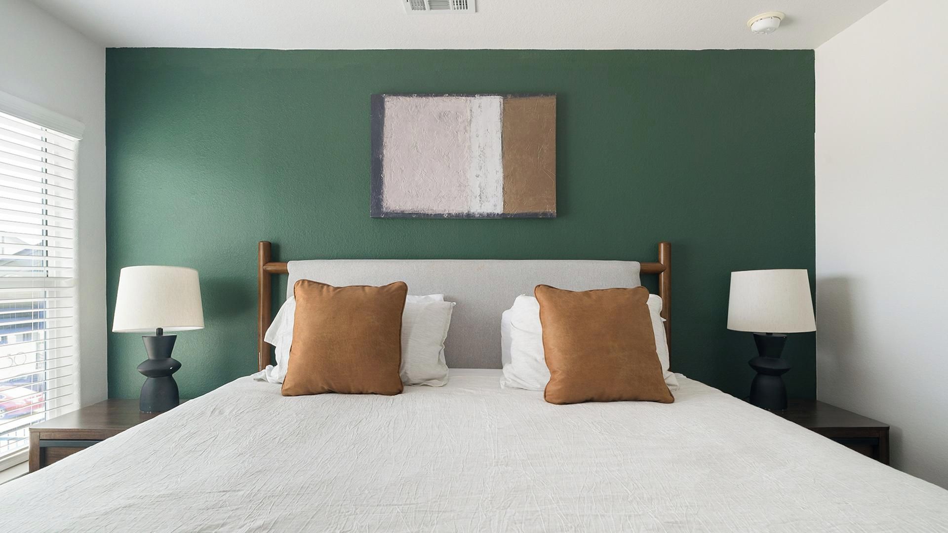 A hotel room with a large bed, two bedside lamps, a green wall, and a ceiling light.
