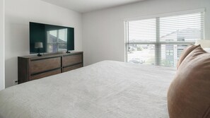 A bedroom with a bed, a dresser, a television on top, and a window with blinds. - Landing | Amazing 1BD, Pool (Houston)