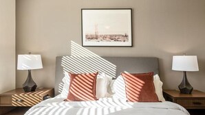 Ein Hotelzimmer mit einem Bett, zwei Nachttischen, zwei Lampen, einem gerahmten Bild an der Wand und gemusterten Kissen.