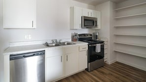A modern kitchen with stainless steel appliances, white cabinetry, and a wooden floor. - Landing | Amazing 1BD, Pool (Houston)
