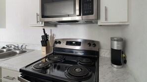 A kitchen with a stove, microwave, and a coffee maker. - Landing | Beautiful 1BD, Pool (Houston)