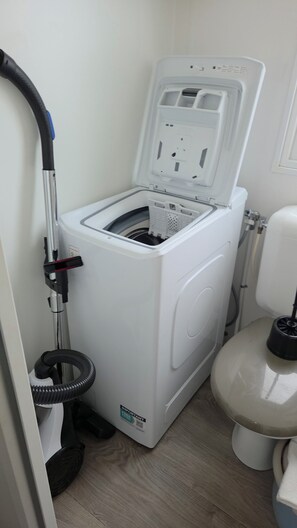 A compact, white laundry machine with a front-loading door, a hose, and a control panel. - The Mar Estang Oasis (Canet-en-Roussillon)