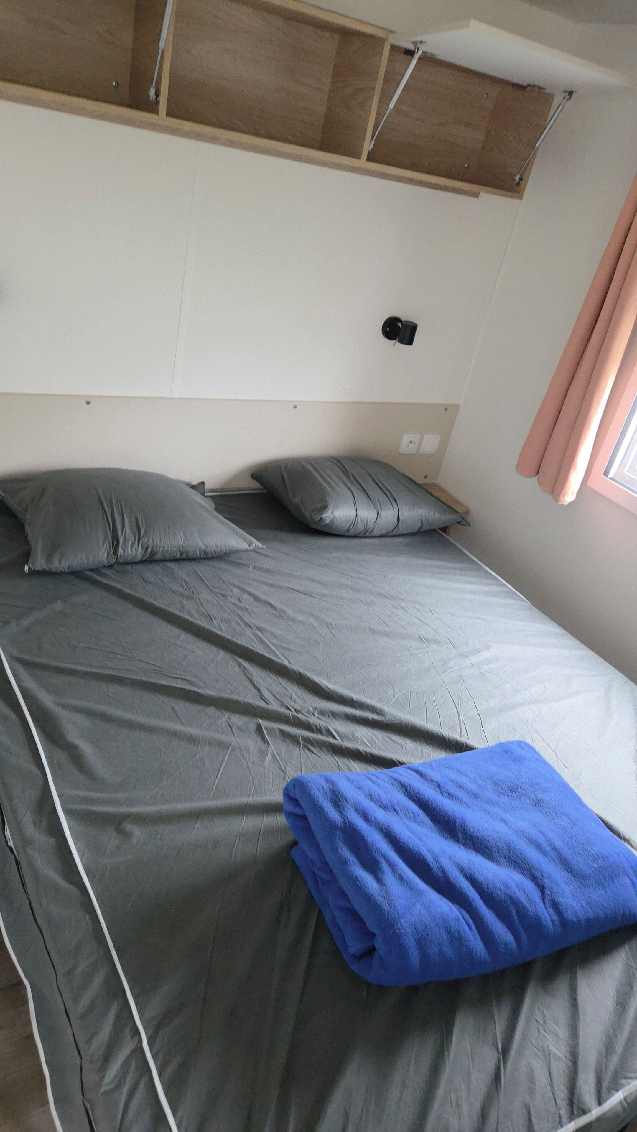A single bed with grey bedding and pillows, a blue towel, and a wooden headboard.