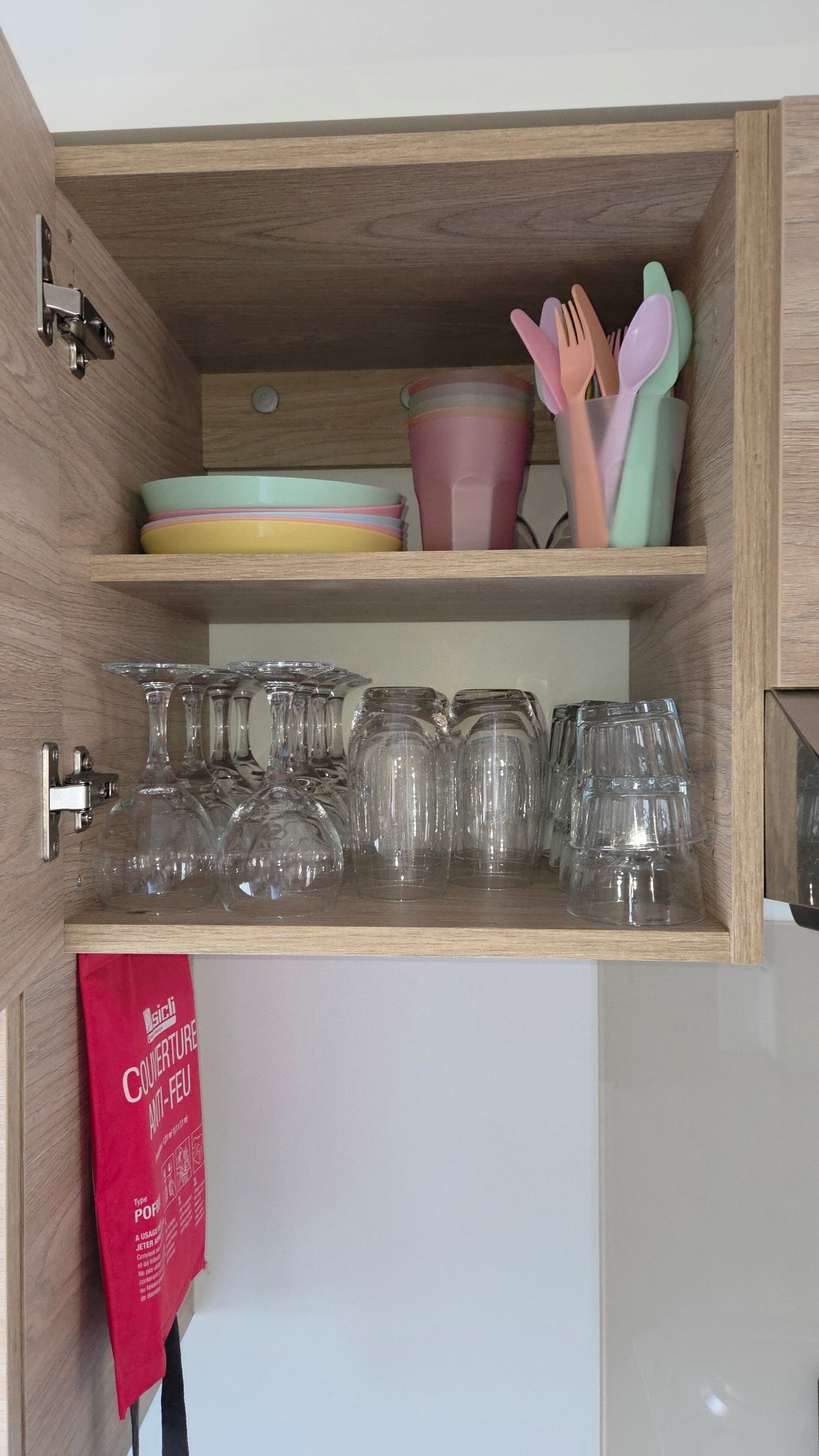 A wooden cabinet with shelves holding glassware and colorful dishware.