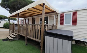 Eine überdachte Terrasse mit Holzwertung, eine kleine Stufe zum Aufgang und ein Mülleimer auf der rechten Seite.