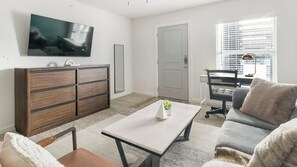 Una sala de estar moderna con una televisión de pantalla plana, un mueble de madera, un sofá, una mesa de centro y una ventana con persianas.
