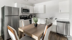Une cuisine moderne dotée d’appareils électroménagers en acier inoxydable, de meubles blancs et d’une table à manger avec des chaises.