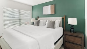 A neatly made bed with white linens, a bedside table with a lamp, and a window with blinds. - Landing | Beautiful 2BD, Pool (Houston)