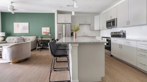 A modern kitchen with white cabinets, a central island, and a dining area with a sofa and chairs. - Landing | Incredible 1BD, Yoga Studio, Gym (Sarasota)