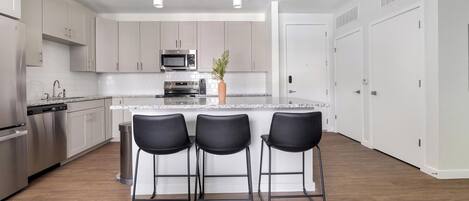 A modern kitchen with stainless steel appliances, a central island with bar stools, and white cabinetry.