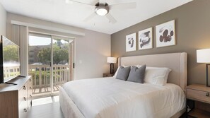 Quarto de hotel com uma cama grande, um ventilador de teto, uma televisão e uma varanda com vista para o exterior.