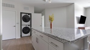 A modern kitchen with granite countertops, a built-in washer and dryer, and a flat-screen TV mounted on the wall. - Landing | Spectacular 1BD, Gym, Yoga Studio (Sarasota)
