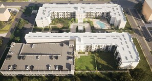 Een meerhoog hotel met zwembad op het dak, een parkeerplaats en aangelegde tuinen.